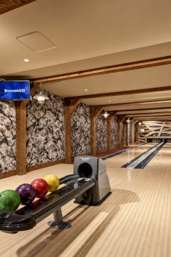 Indoor bowling lane with Brunswick screens, wooden beams, and colorful bowling balls, stretching down the hallway.