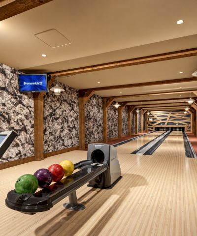 Indoor bowling lane with Brunswick screens, wooden beams, and colorful bowling balls, stretching down the hallway.