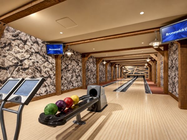 A modern bowling alley with wooden lanes, Brunswick screens, and colorful bowling balls in the foreground.