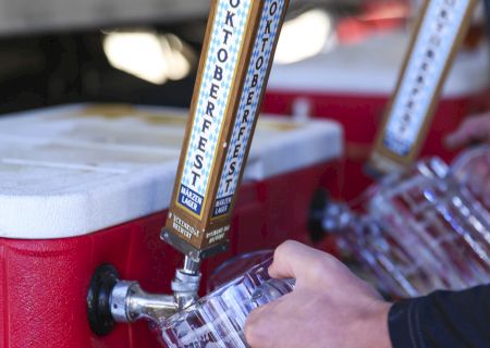 A hand pours beer from a red draft tap with a wooden label at a brewery event.